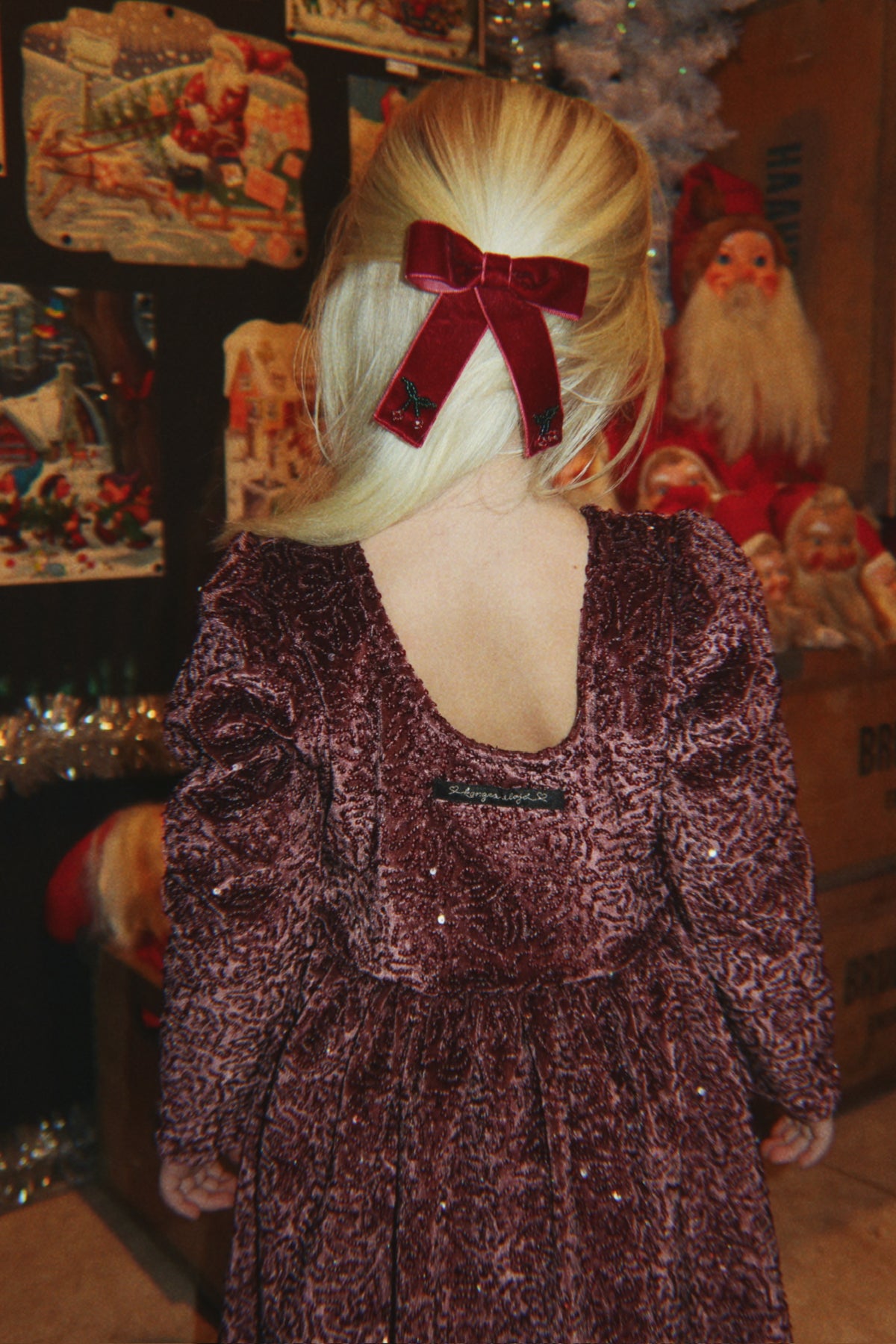 Child wearing a red velvet bow with cherry embroidery and a plum textured dress