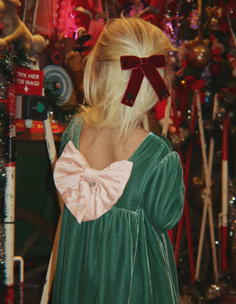 Girl in a green velvet dress with a pink bow at Christmas