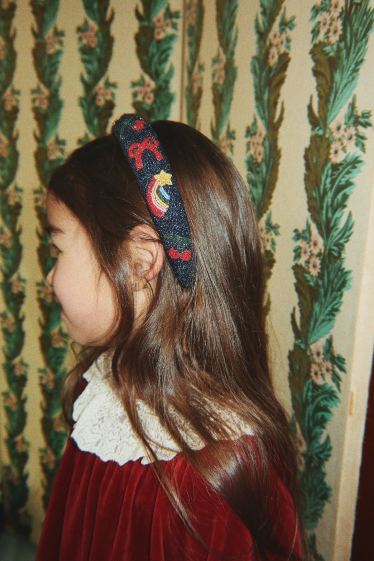 Child in a red velvet dress with a lace collar and embroidered navy headband