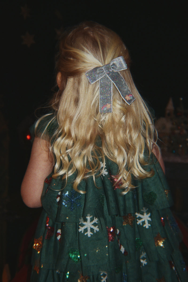 Child wearing a green sequin party dress and silver embroidered bow hair clip